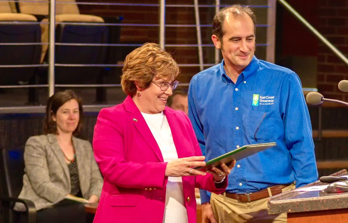 in 2019, Lori Bush reads a proclamation honoring National Bike Month and the East Coast Greenway before presenting it to Executive Director Dennis Markatos-Soriano.